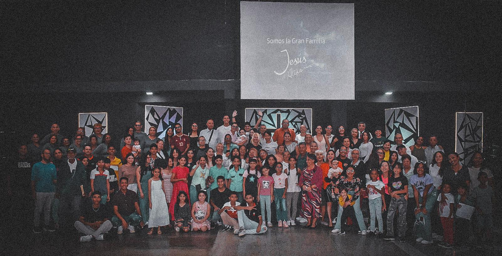 Gran familia cristiana reunida con pantalla mostrando "Somos la Gran Familia Jesús El Altísimo"