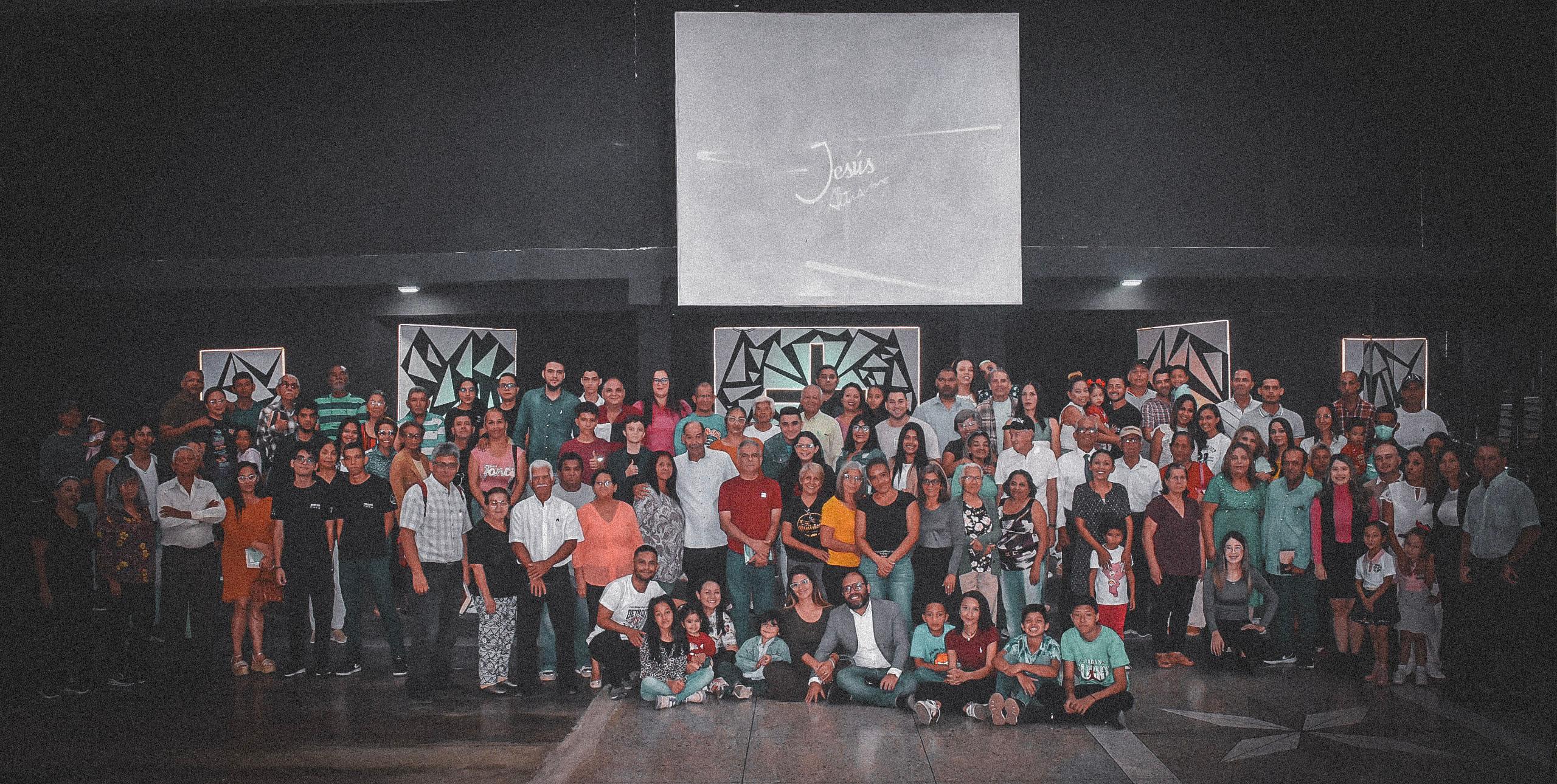Congregación diversa de creyentes con pantalla central mostrando "Jesús El Altísimo" en auditorio moderno